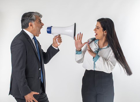 Furious and frustrated senior businessman shouting at female colleague through megaphone against white background