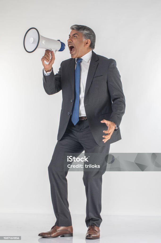 Angry professional screaming into megaphone on white background Angry senior male professional dressed in suit screaming into megaphone while standing against white background Adult Stock Photo