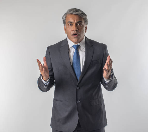 Portrait of worried and shocked senior businessman dressed in elegant suit gesturing while standing against white background