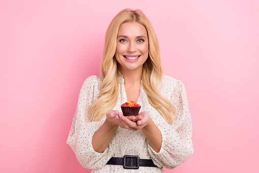 Photo portrait of pretty blonde female hold sweet maffin tasty food wear trendy white outfit isolated on pink color background.