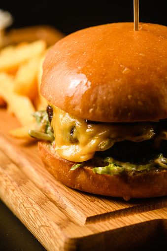 Appetizing burger with french fries on a wooden cutting board, close-up.