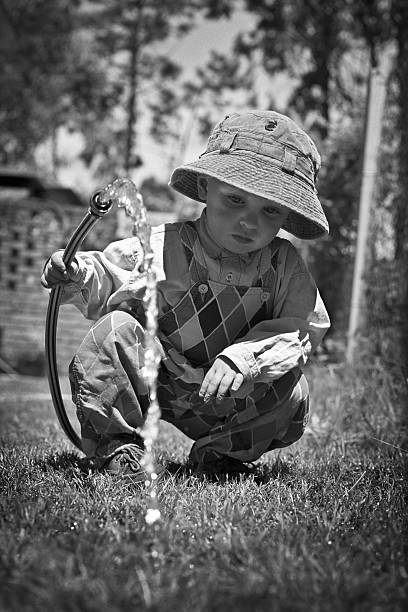 little boy crouched watering grass stock photo