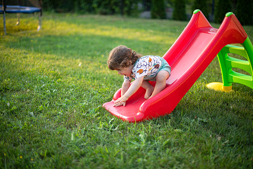 Cute baby boy sliding at his backyard playground