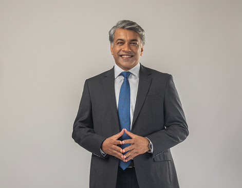 Portrait of confident professional businessman dressed in elegant suit with hands clasped standing against white background