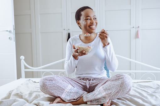 A young woman is eating breakfast at home and enjoying in bedroom