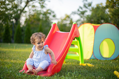 Cute baby girl sliding at a backyard playground,