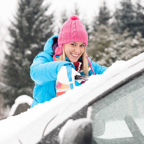 Woman cleaning car windshield of snow winter stock photo
