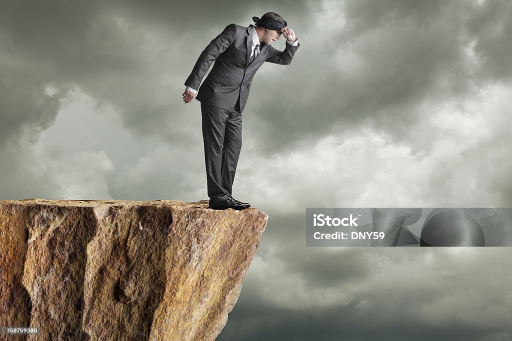 Peaking A businessman peaking out from his blindfold while standing at the edge of a cliff. Cliff Stock Photo