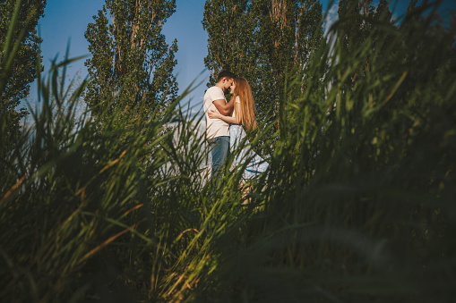 View through the grass of a couple standing face to face, before they kiss. Love story and countryside adventure