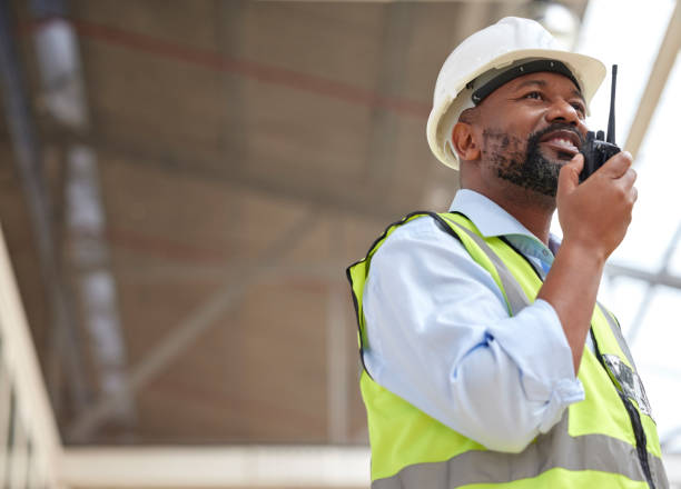 istock Walkie talkie, black man and engineer planning, communication and construction. African architect, radio and happy contractor with industrial project, building maintenance and engineering discussion. 1587635344