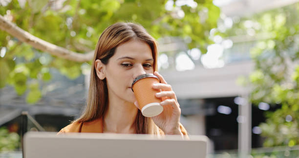 Caucasian businesswoman sitting at work wearing headphones Online meeting via laptop alone in the park. Woman drinking coffee alone in summer cafe stock photo