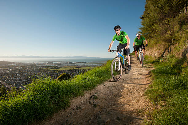 Cycling Above Nelson Two cyclists speed down a track above nelson, New Zealand nelson city new zealand stock pictures, royalty-free photos & images