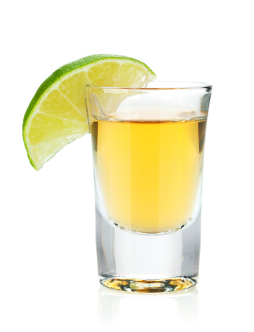 Shot of gold tequila with lime slice. Isolated on white background