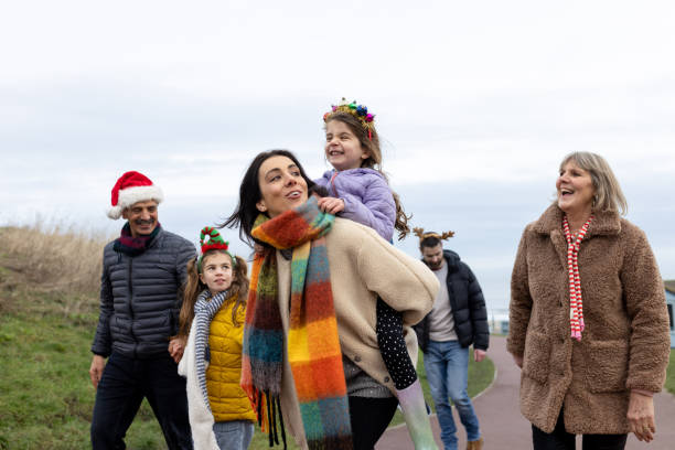 Three-quarter length shot of a multi-generational family walking together on Christmas day. They are all wearing warm clothing laughing and talking together. The youngest daughter is on her mother's back.