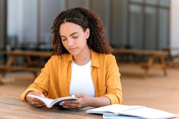 istock Calm concentrated brazilian or hispanic curly haired female student, sit outdoors with a book in her hands, focused reading interesting book, gain information, get inspired. Reading concept 1587713498