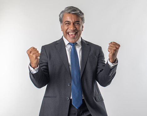 Portrait of elegant senior businessman screaming cheerfully and shaking fists while celebrating success against white background