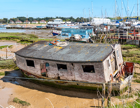 A derelict old wooden houseboat moored in the mudflats beside the River Deben at Felixstowe Ferry in Suffolk, Eastern England. The tiny hamlet of Bawdsey is on the opposite bank of the river.