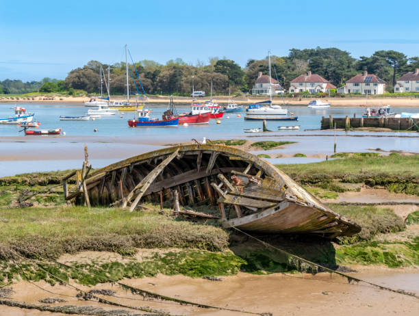 An abandoned wooden boat decaying in the mudflats beside the River Deben at Felixstowe Ferry in Suffolk, Eastern England. The tiny hamlet of Bawdsey is on the opposite bank of the river.