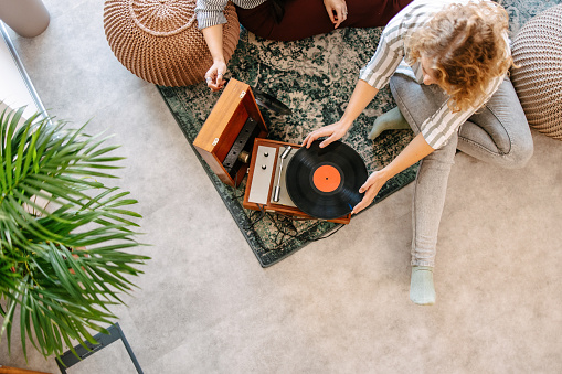 High-angle view of female friends listening to old records and smiling. Vinyl