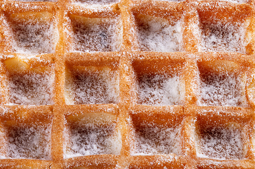 Macro shot of a belgian waffle sprinkled with powdered icing sugar