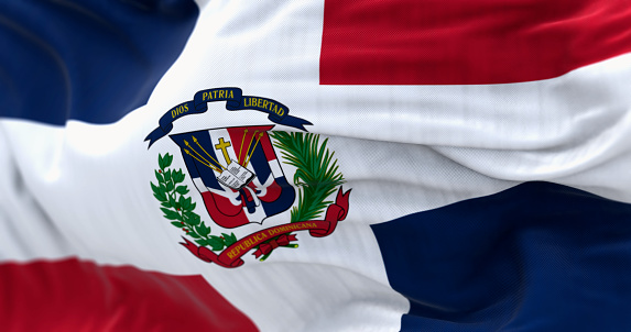 Close-up of the Dominican Republic flag waving. Red and blue flag with white cross, coat of arms in center. 3d illustration render. Rippled fabric. Textured background. Selective focus