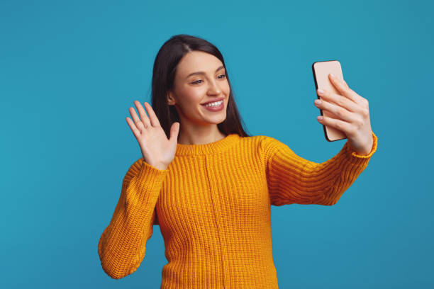istock Cute young attractive woman waving while having video-call, isolated over blue background 1587794907