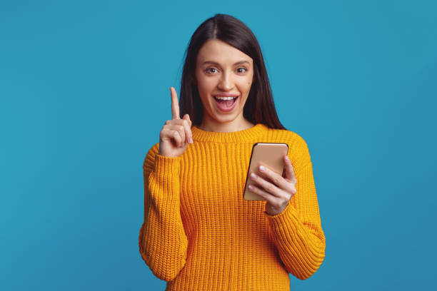 istock Smiling young woman holds modern cellular, sends message in social networks while pointing up 1587796060