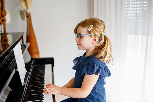 Little girl playing piano,facing camera and smiling. She's about 9 years old of which two years in piano lessons. She's wearing pink t-shirt, has green bow in her hair looking over her shoulder