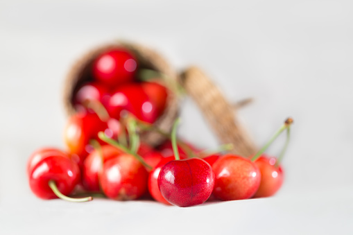 Close-up of a tasty red cherry. Behind it is a group of cherries sticking out of a wicker basket.