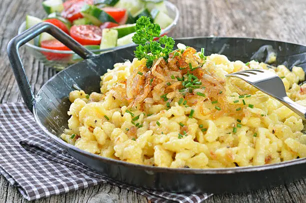 Southern German cheese noodles with fried onion rings in a serving pan, with side salad