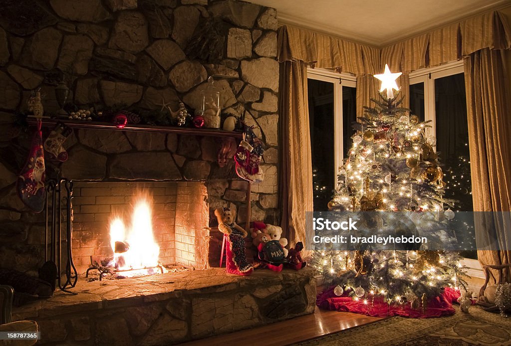 Christmas tree and stone fireplace in a cozy vintage home A beautifully decorated christmas tree, dressed with christmas tree lights and a star atop, is placed in the corner of a vintage styled model home. A rustic stone fireplace contains a roaring log fire to warm the cozy interior of the home. The room is lit purely by the fire and the christmas lights to create the warm, romantic and cozy mood. Christmas Stock Photo