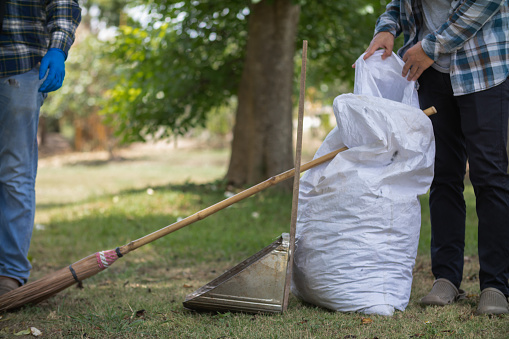 White sacks are used to contain dead leaves that have fallen seasonally in spring as way to clean park and mix  leaves to make compost. coconut broom sits next to powder scoop and sack for dry leaves.