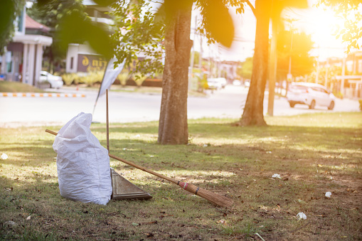White sacks are used to contain dead leaves that have fallen seasonally in spring as way to clean park and mix  leaves to make compost. coconut broom sits next to powder scoop and sack for dry leaves.