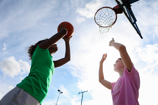 Throwing ball in a jump. Portrait of teen girl in blue uniform training, playing basketball isolated over white background. Concept of sport, active lifestyle, health, team game and ad