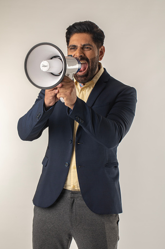 Angry senior male screaming into megaphone while standing against white background