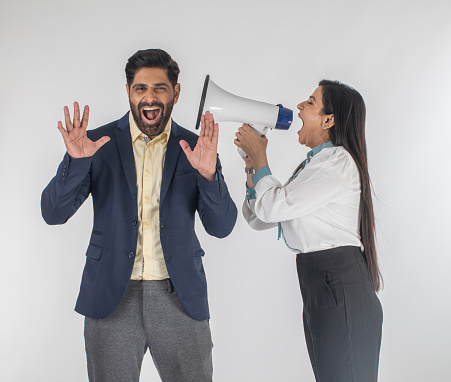 Furious and frustrated senior businesswoman shouting at male colleague through megaphone against white background