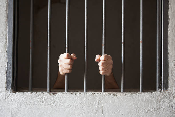 istock A prisoner grips the bars from inside a dark cell 158791810