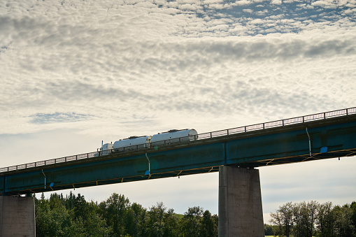 Low angle view of a tanker truck driving across a bridge in some scenic countryside during a long haul delivery