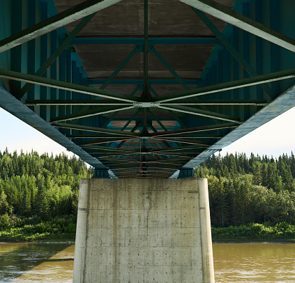 View of the underside of a large multi-lane bridge stretching across a river in scenic countryside