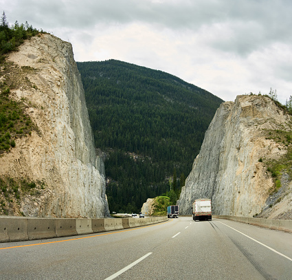 Cars and trucks driving along a multi-lane highway carved through rocks running through scenic countryside