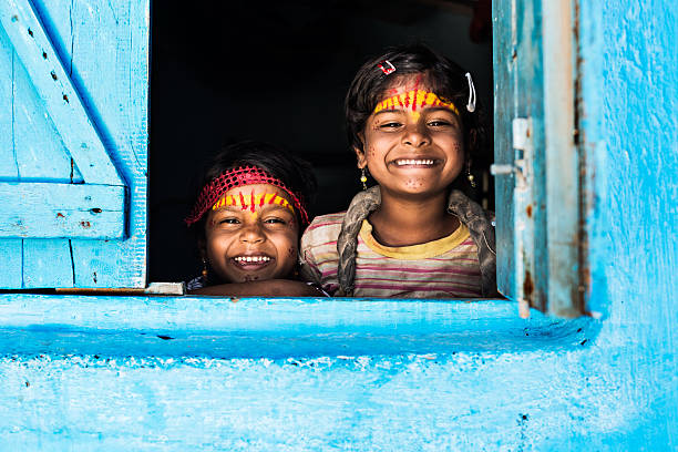 Welcoming faces Two little Indian sisters smiling on the window of their blue house. mumbai stock pictures, royalty-free photos & images