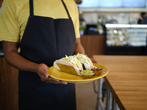 A food server in a restaurant holding a plate of tacos.