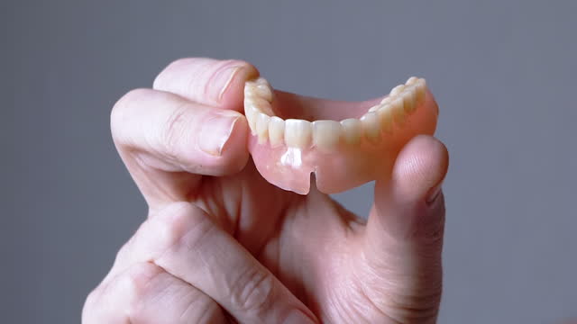 Hand Elderly Holding a Removable Upper Jaw Denture on a Blurred Background