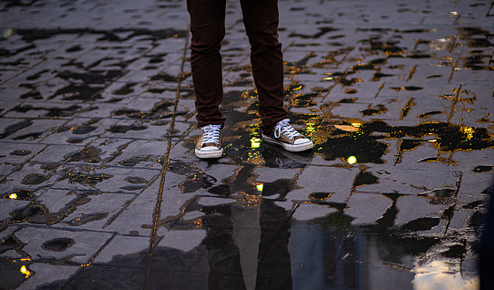 Standing thin young man's legs reflected in bulbous, circular bokeh of rainwater trapped on the cement floor. in the lonely night