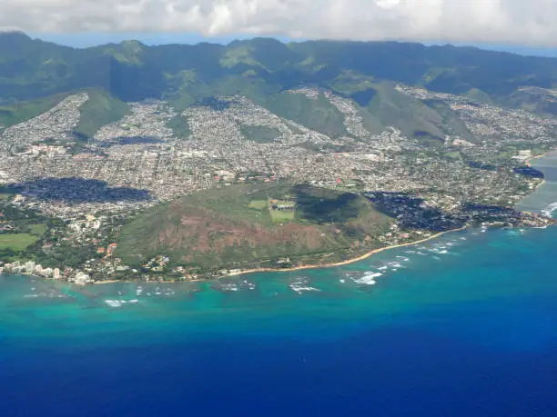 A view of the aerial view of Diamondhead, a volcanic cone and a popular hiking destination, and other areas on Oahu, Hawaii, on October 15, 2019. The view shows the contrast between the urban and natural landscapes of the island. The areas of Kapahulu, a residential and commercial neighborhood, and Kahala, an affluent and secluded area, are also visible. The Pacific ocean is blue and sparkling in the sunlight.