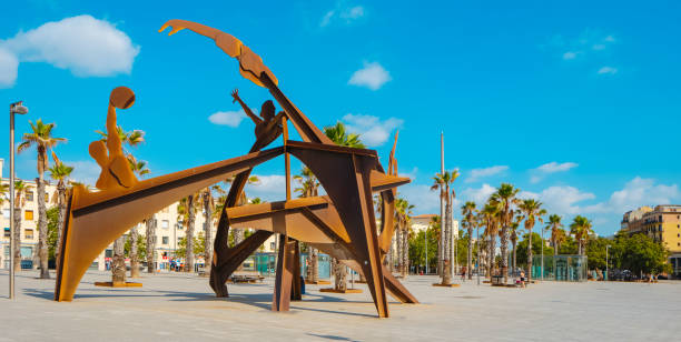 Barcelona, Spain - July 27, 2023: Panoramic view of Placa del Mar square, in La Barceloneta, Barcelona, Spain, with the Homenatge a la Natacio sculpture on the left in the foreground