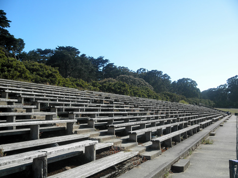 Old wooden bleachers in Golden Gate Park, San Francisco, California. The bleachers are surrounded by green grass and trees, and have a vintage charm.