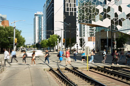 Unrecognizable group of people in blurred motion crossing a street by railroad tracks in a city with modern architecture