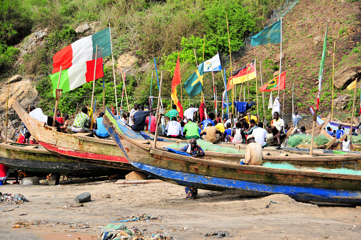 Abandze / Kormantin, Mfantseman District, Central Region, Ghana, West Africa: fishermen and traditional wooden fishing boats decorated with assorted flags - Gulf of Guinea, Atlantic Ocean.