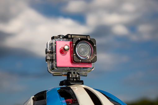 Action camera in a protective box on a bicycle helmet against a blue sky background.